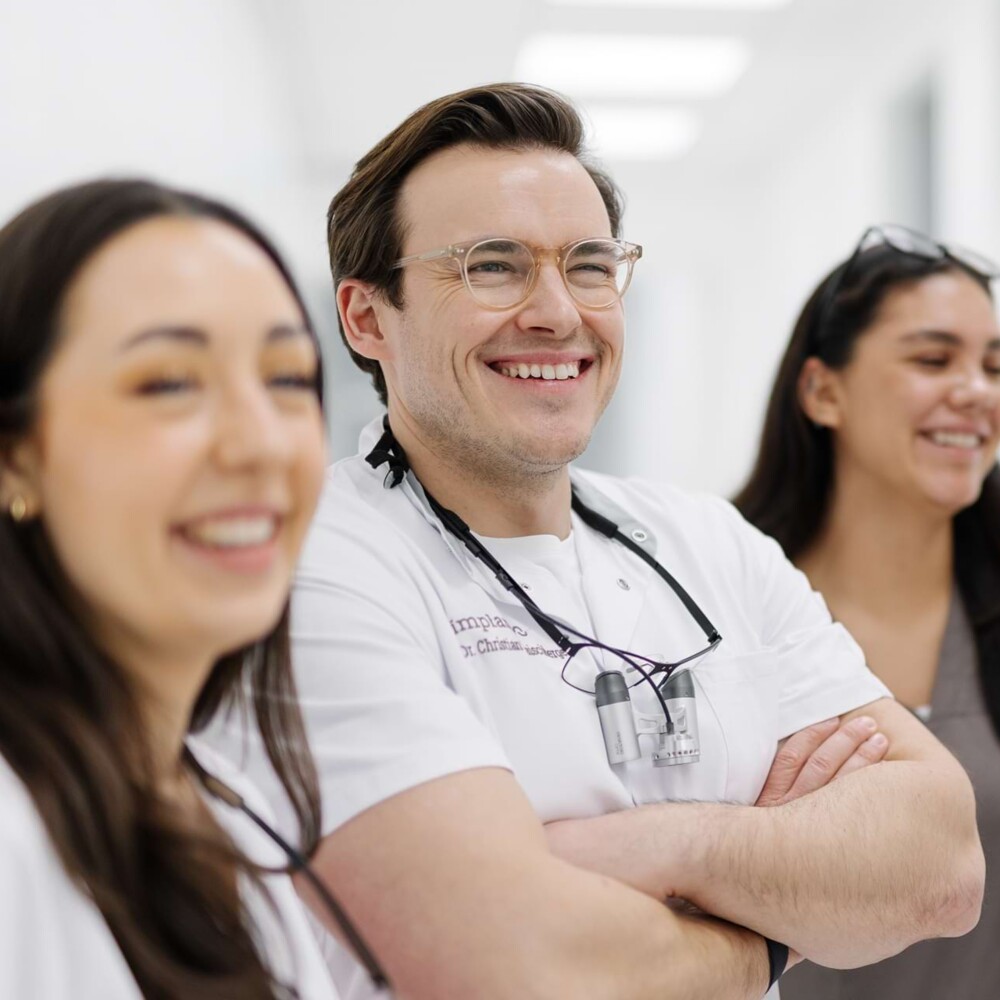 Drei Behandler:innen der Dental Clinic implaneo stehen im Gang und lachen